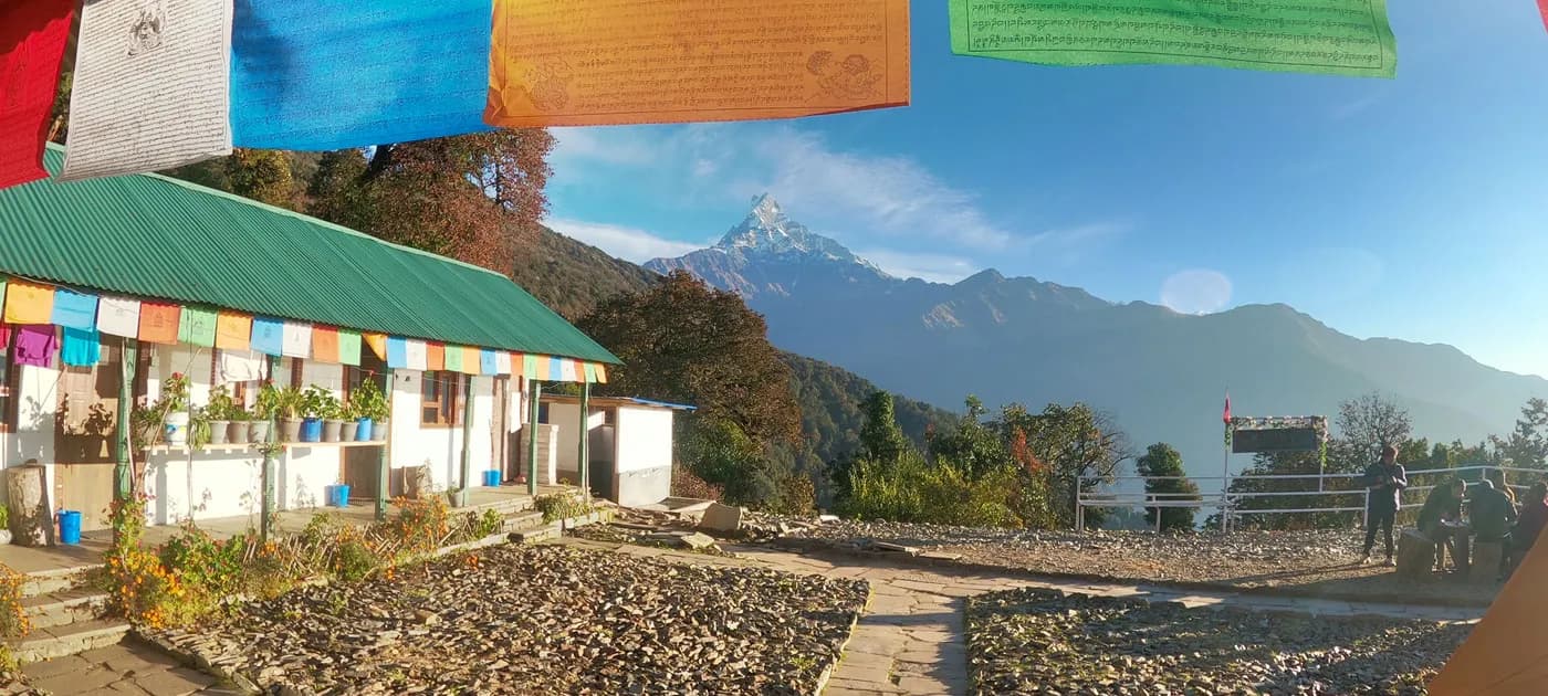 A scenic mountain tea house decorated with colorful prayer flags offering clear views of Mount Machhapuchhre in the background.