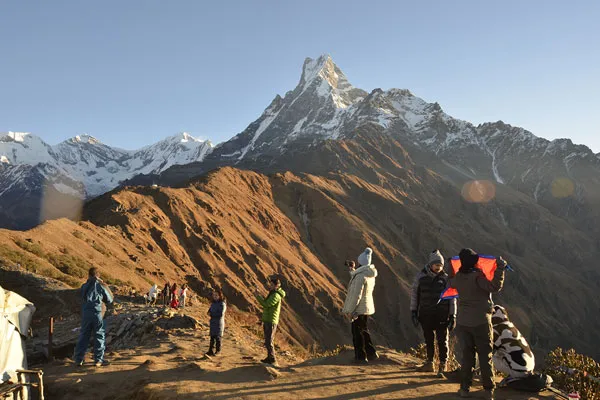 A group of trekkers taking photos on a high mountain ridge overlooking the prominent fishtail peak of Mount Machhapuchhre in Nepal