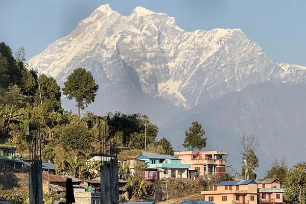 A hillside village with traditional colorful homes set beneath the massive snow-capped peak of Mount Gaurishankar.