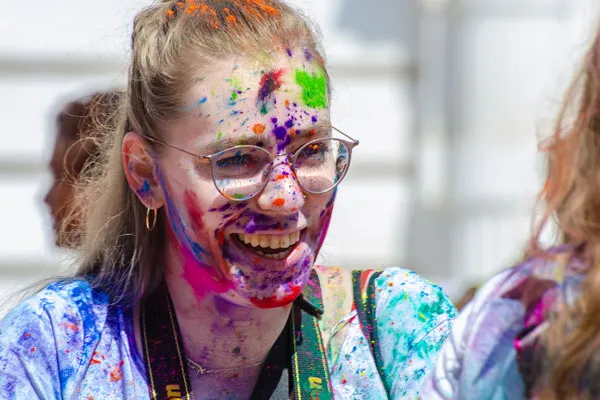 A smiling young woman wearing glasses with colorful powder splashes across her face during the Holi festival in Nepal