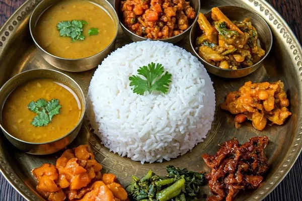 Authentic Nepali Dal Bhat thali set served on a brass plate with rice, lentil soup, curry, green spinach, and vegetable pickles.
