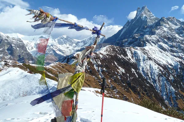 Buddhist prayer flags blowing in the wind on a snowy high ridge overlooking Machhapuchhre mountain peak