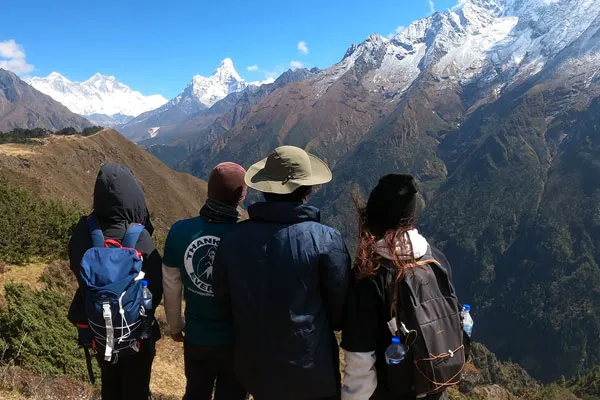 Four travelers with backpacks standing on a mountain ridge looking out at Mount Everest, Lhotse, and Ama Dablam in Nepal