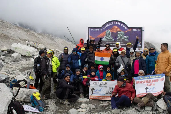 A large group of Indian trekkers gathered in front of the official Everest Base Camp sign board holding the national flag of India and banner.