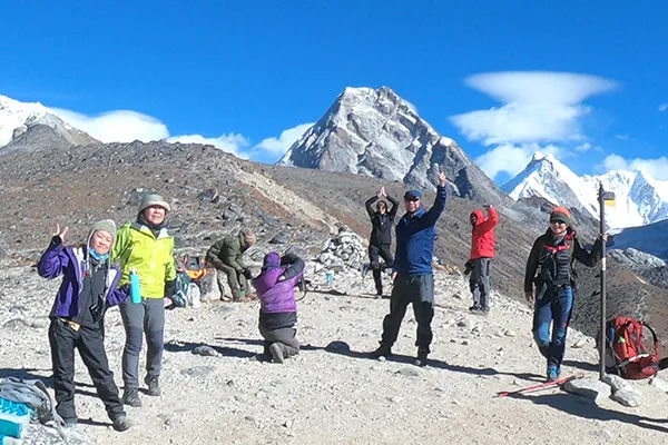 An international group of yoga trek participants and instructor practicing standing yoga poses together on an open field in front of Tengboche Monastery.