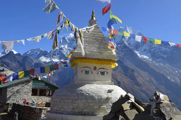 A white Buddhist stupa decorated with Buddha eyes and colorful prayer flags against the backdrop of snow-covered Mount Ama Dablam in the Everest region.
