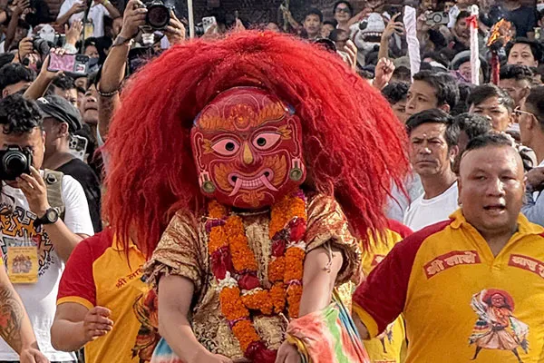 A performer wearing the iconic red wrathful Majipa Lakhey mask with long red hair and marigold garlands performing amidst crowds in Kathmandu.