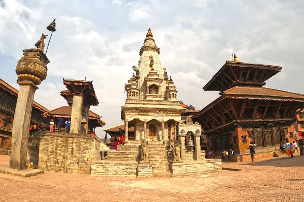 istoric stone temple and traditional pagoda architecture surrounding Bhaktapur Durbar Square under a cloudy sky.