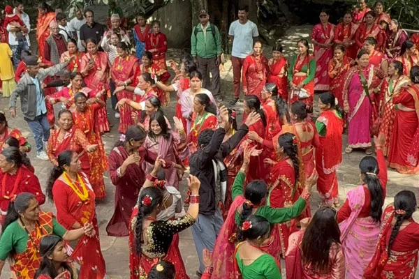 Nepalese women wearing traditional red saris and red attire gathering outdoors and dancing together during the Hartalika Teej festival.