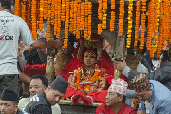Close-up of the Living Goddess Kumari dressed in traditional red and gold attire, seated inside a chariot decorated with yellow and orange marigold garlands during Indra Jatra.