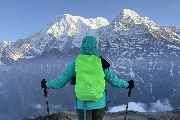 A trekker with a bright green backpack cover standing on a high ridge facing the majestic snow-covered Mardi Himal and Annapurna peaks