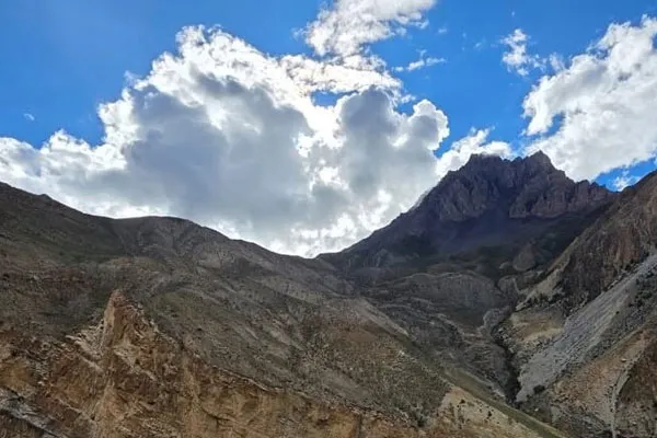 A rugged and arid mountain landscape with steep rocky cliffs and clouds overhead on the Namun La Pass trekking route in Nepal.