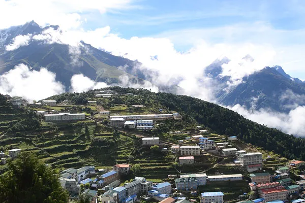 An aerial view of the terraced mountain village of Namche Bazaar with colorful teahouses built into the hillside under clouds