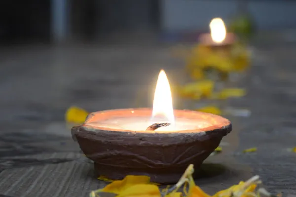 A close-up shot of a lit traditional clay oil lamp (diyo) surrounded by scattered yellow marigold flower petals during Tihar festival.