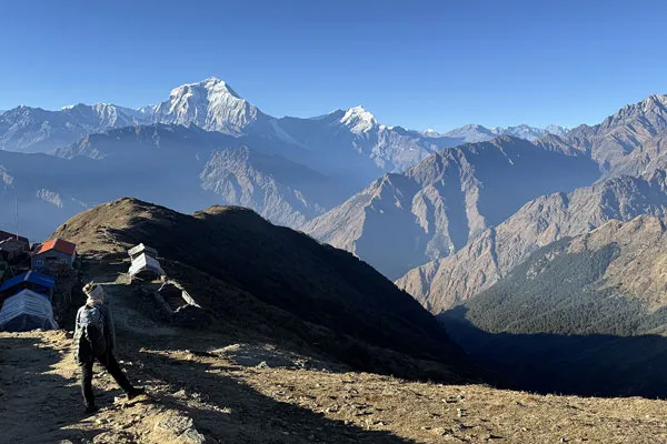 A solo trekker standing on a high grassy ridge overlooking vast Himalayan mountain ranges