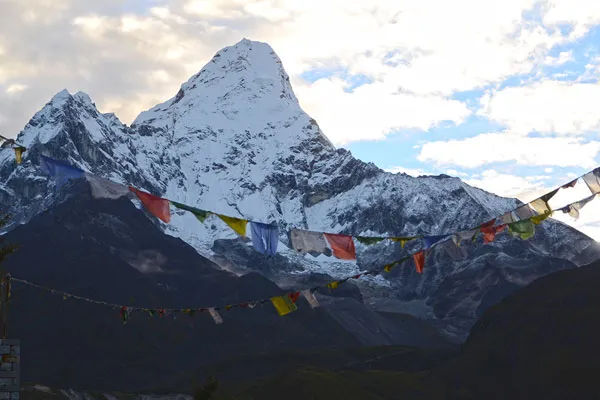 Colorful Buddhist prayer flags stretched across a clear sky with the distinct sharp peak of Mount Ama Dablam in the background