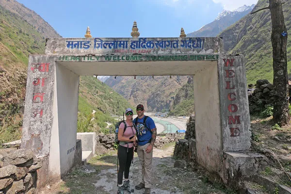 Trekking couple standing under the stone welcome gate to Manang District during a bright day on the Annapurna Circuit trail.