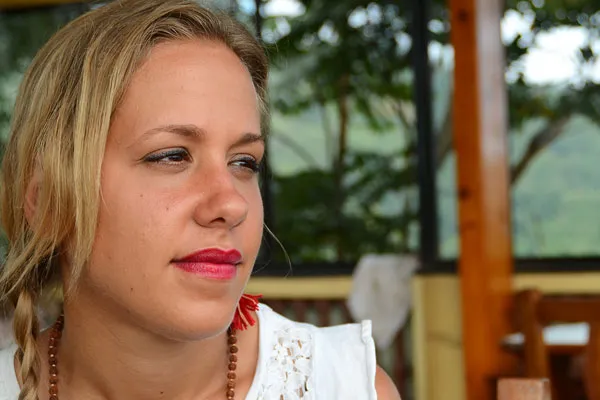 Close-up portrait of a female traveler with braided hair and red lipstick looking thoughtfully out from a mountain teahouse