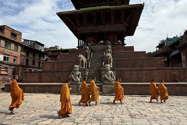 Buddhist monks wearing traditional orange robes walking across the stone-paved Taumadhi Square in front of the multi-tiered Nyatapola Temple in Bhaktapur, Nepal