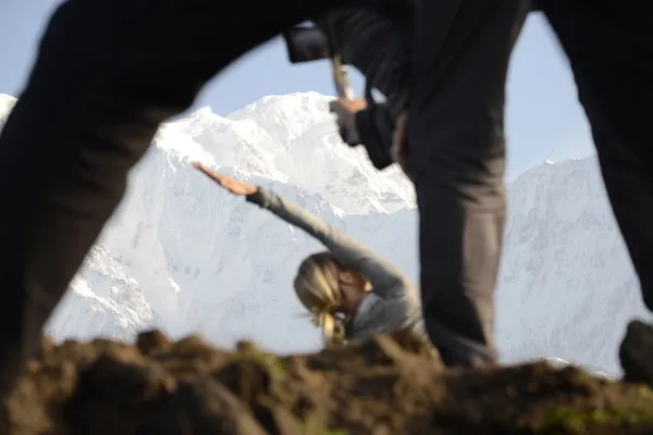 A person practicing a outdoor yoga pose framed in the foreground with snow-capped Himalayan mountain peaks in the background.