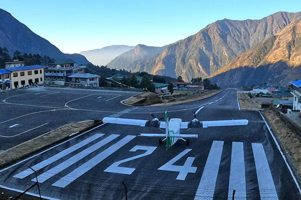 A small prop plane positioned on the sloped runway at Lukla Airport with steep mountain peaks in the background