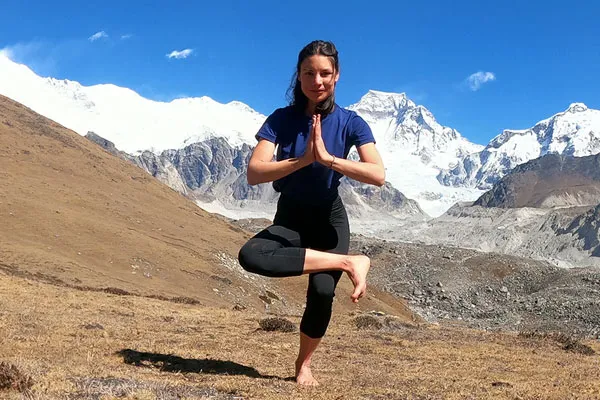 Woman performing a balancing yoga pose outdoors with majestic snow-covered Himalayan peaks in the background