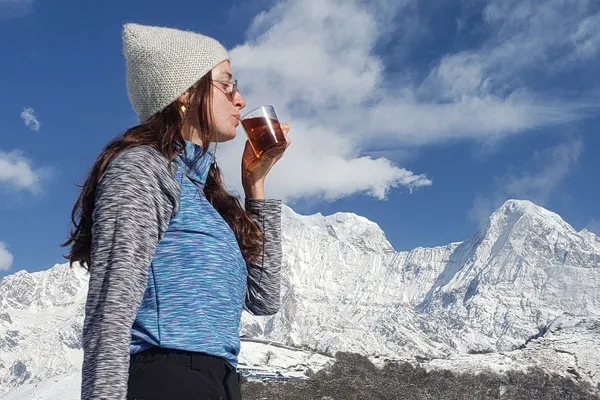Female trekker enjoying hot tea with snow-capped Annapurna mountains in the background, representing best winter destinations in Nepal.