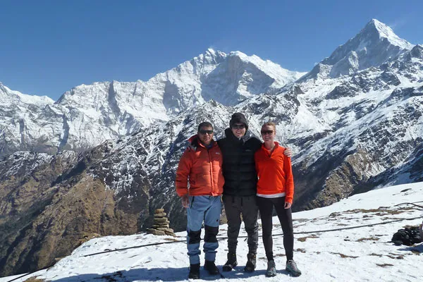 Three trekkers posing together on a snowy trail with Himalayan peaks in the background during a Nepal winter trek.
