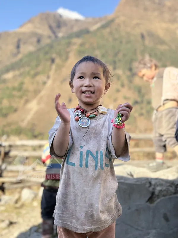 A young smiling child wearing traditional necklaces outdoors in a rural mountain village in Nepal.