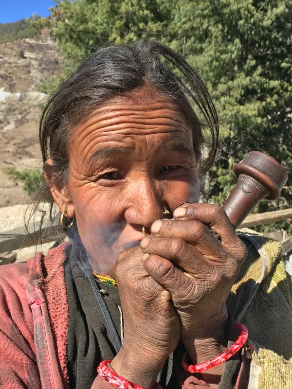 Close-up vertical portrait of an elderly indigenous Nepalese woman holding and smoking a traditional wooden pipe in a remote mountain village.