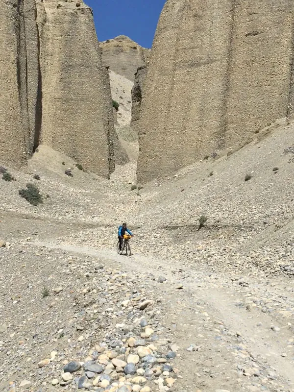 A mountain biker riding through a narrow gravel canyon in the Mustang region of Nepal.