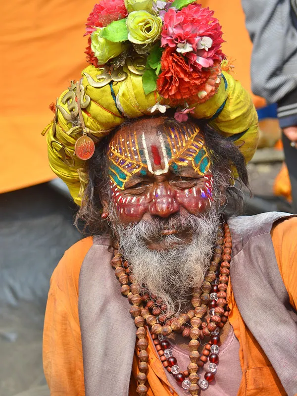 A colorful Hindu Sadhu (holy man) wearing traditional facial paint, rudraksha beads, and a yellow headwrap during an Ancient Hinduism Day Tour in Kathmandu, Nepal