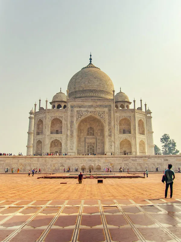Vertical shot of tourists admiring the iconic white marble dome of the Taj Mahal in Agra, India.