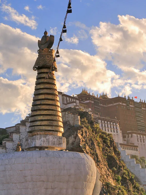 Close-up of a traditional Tibetan Buddhist stupa with prayer bells in front of Potala Palace on a clear day.