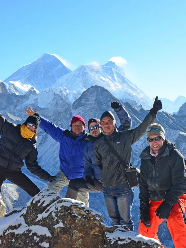 Group of happy trekkers posing together on a snowy ridge with Mount Everest towering in the background