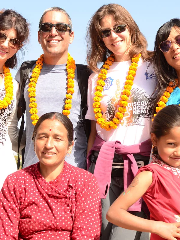 Close-up portrait of international tourists wearing traditional marigold flower garlands alongside their local host family in Nepal.