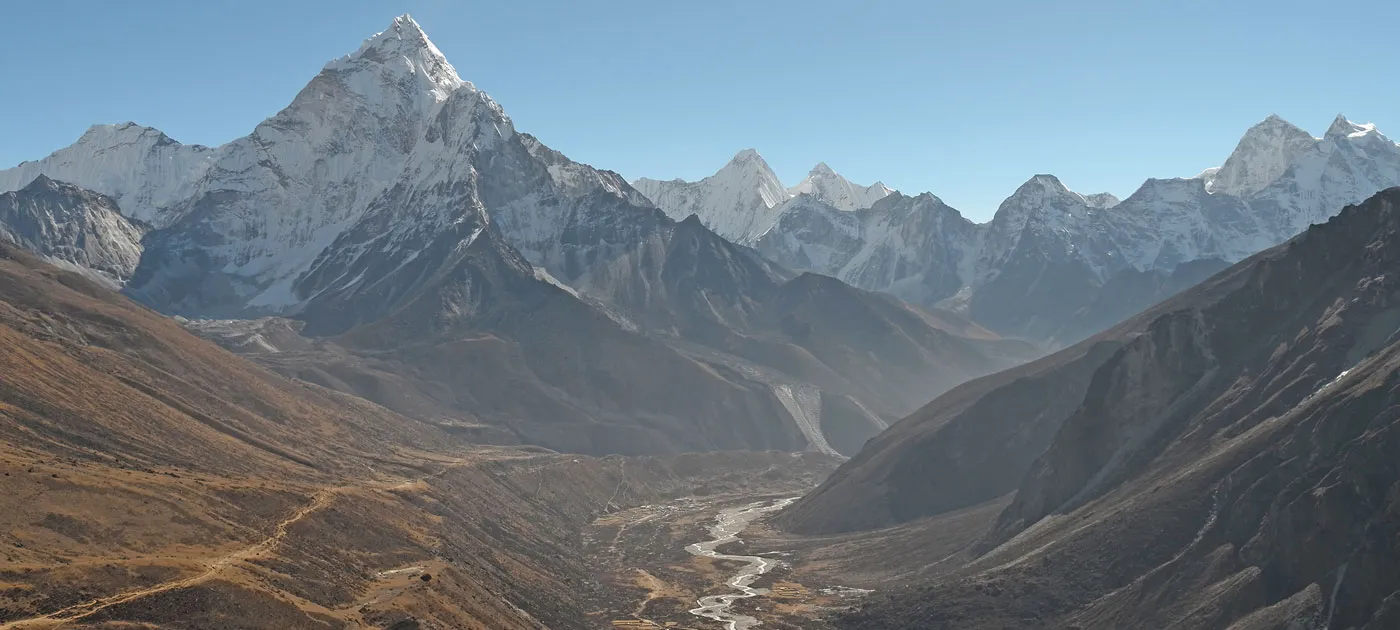 A panoramic vista of Mount Ama Dablam and surrounding Himalayan peaks overlooking a winding glacial river valley along the Everest 3 Passes Trek.
