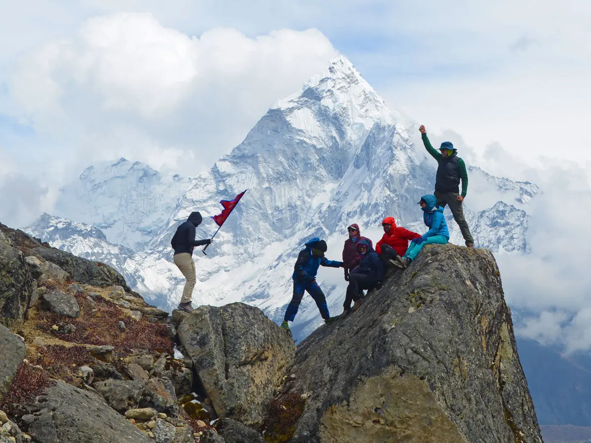 Trekkers posing on rocky outcrop with Nepal flag in front of Mount Ama Dablam.