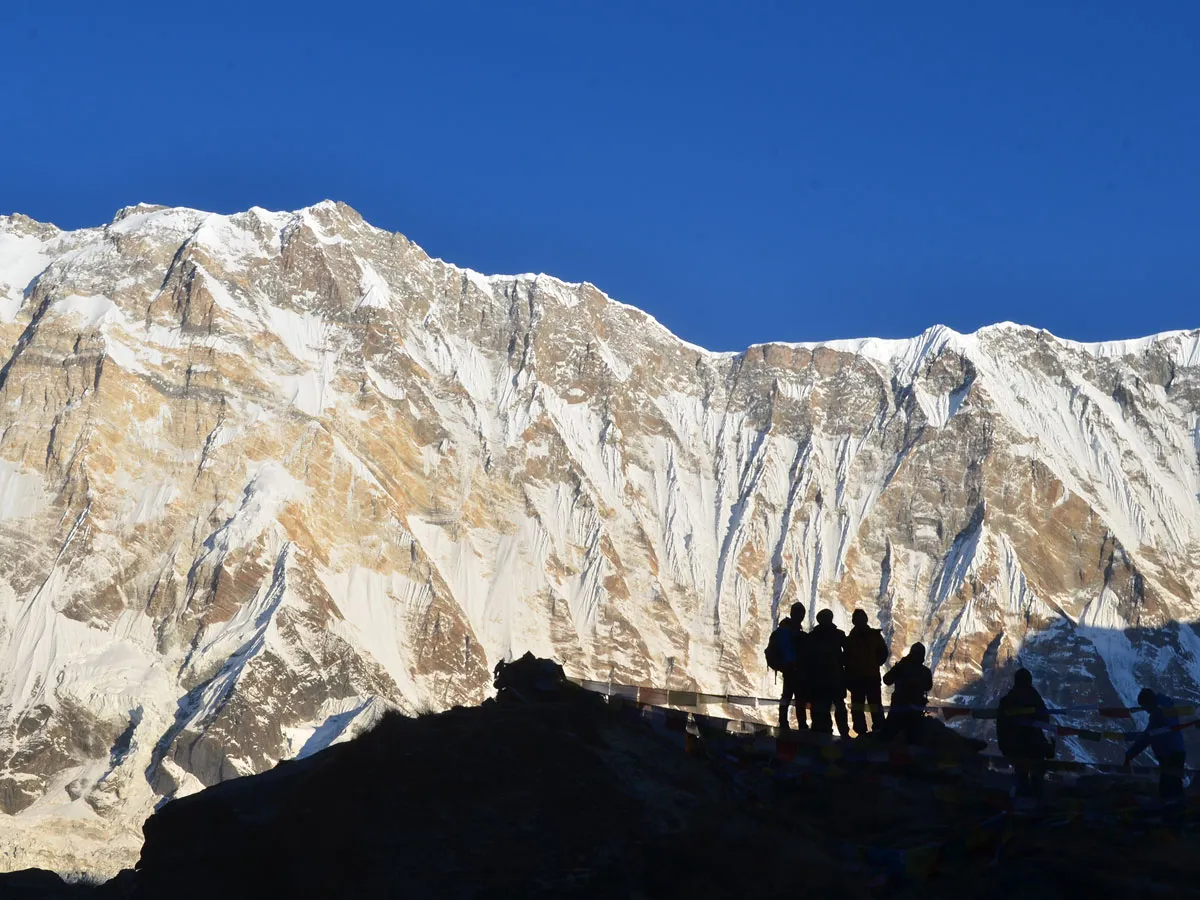 Trekkers standing at Annapurna Base Camp with giant snow covered Himalayan peak in background