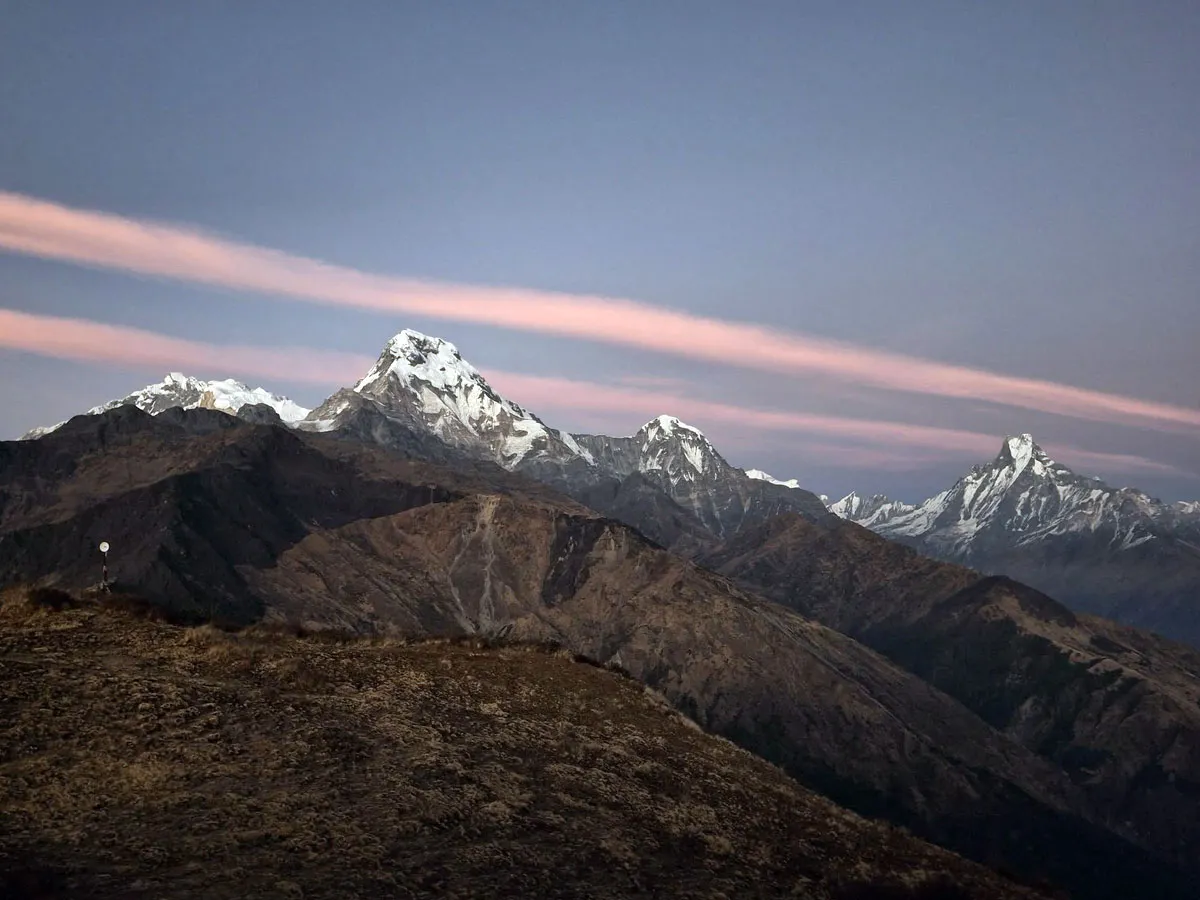 Panoramic view of the snow-capped Annapurna mountain range under a dusk sky with soft pink clouds