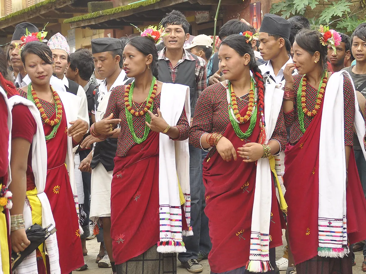 Local Nepalese women and men dressed in vibrant traditional red attire and colorful bead jewelry participating in a cultural celebration during the Royal Trek.