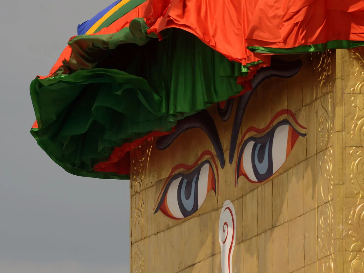Close-up of the iconic wisdom eyes painted on a golden stupa structure adorned with colorful pleated cloth in Nepal.