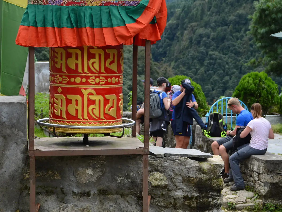Large red Buddhist prayer wheel with trekkers resting nearby