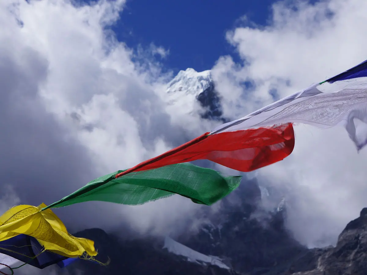 Colorful Buddhist prayer flags fluttering in the wind with a snow-capped Himalayan peak behind clouds