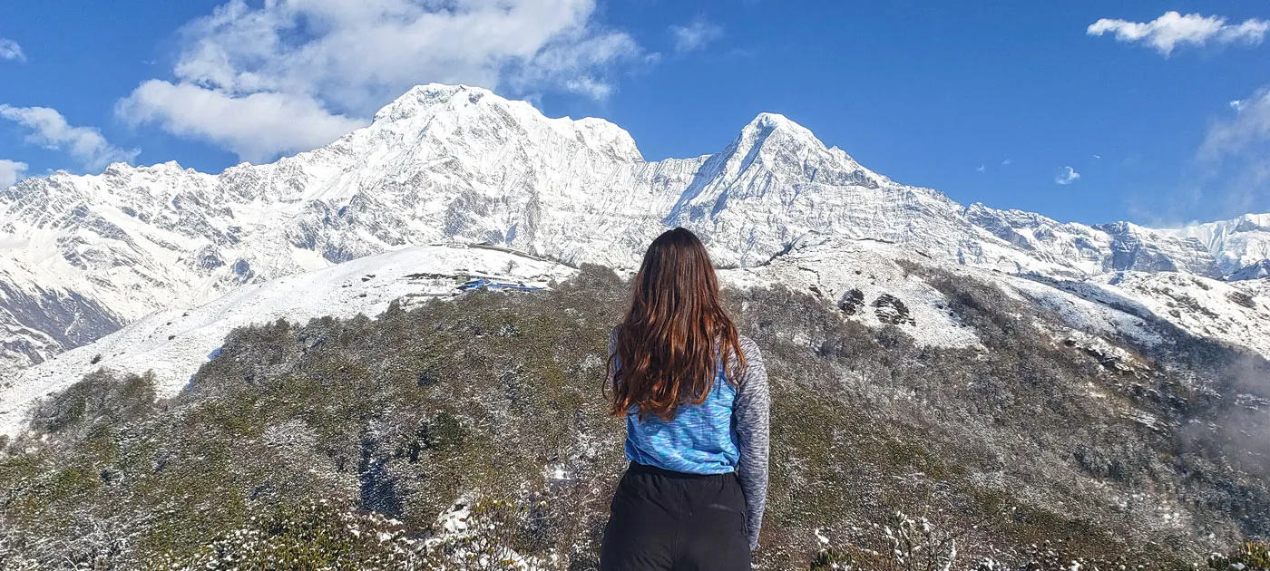 A female trekker seen from behind looking out at the snow-covered Annapurna massifs
