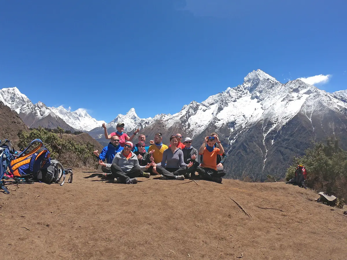 Group of happy trekkers sitting together on a mountain ridge in front of Mt. Ama Dablam.