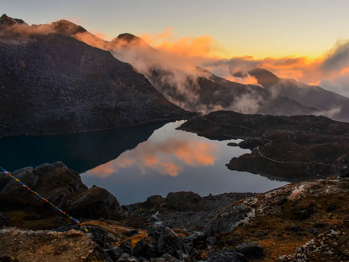 Sacred Gosaikunda alpine lake reflecting golden sunset clouds and surrounding rocky mountain peaks in Nepal.