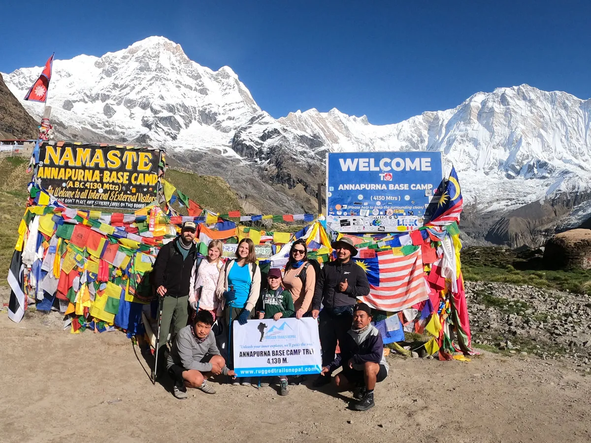 Group of happy trekkers posing with a Rugged Trails Nepal banner at the Annapurna Base Camp signpost