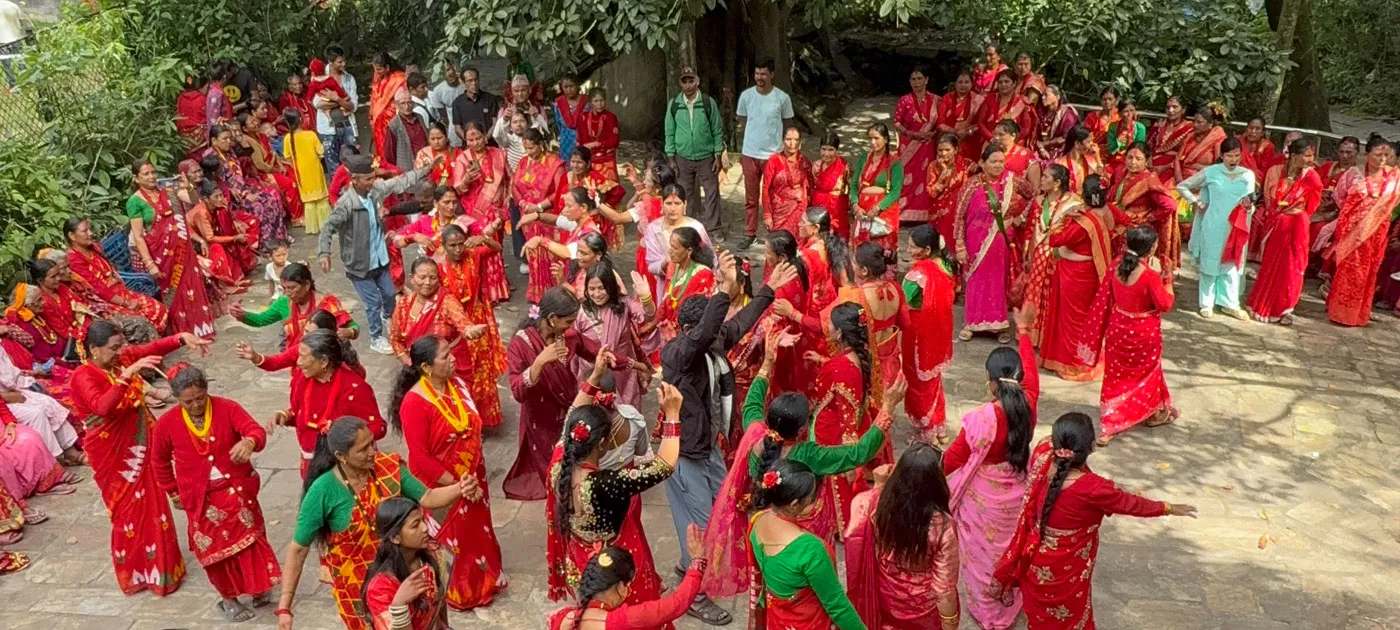A high-angle wide view of a large group of Nepalese women in vibrant red saris celebrating and dancing in a courtyard area