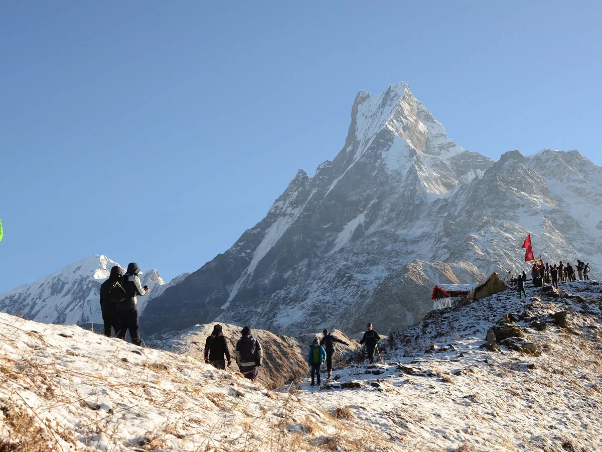 Trekkers walking on a snowy ridge towards the towering peak of Mount Machhapuchhre Fishtail